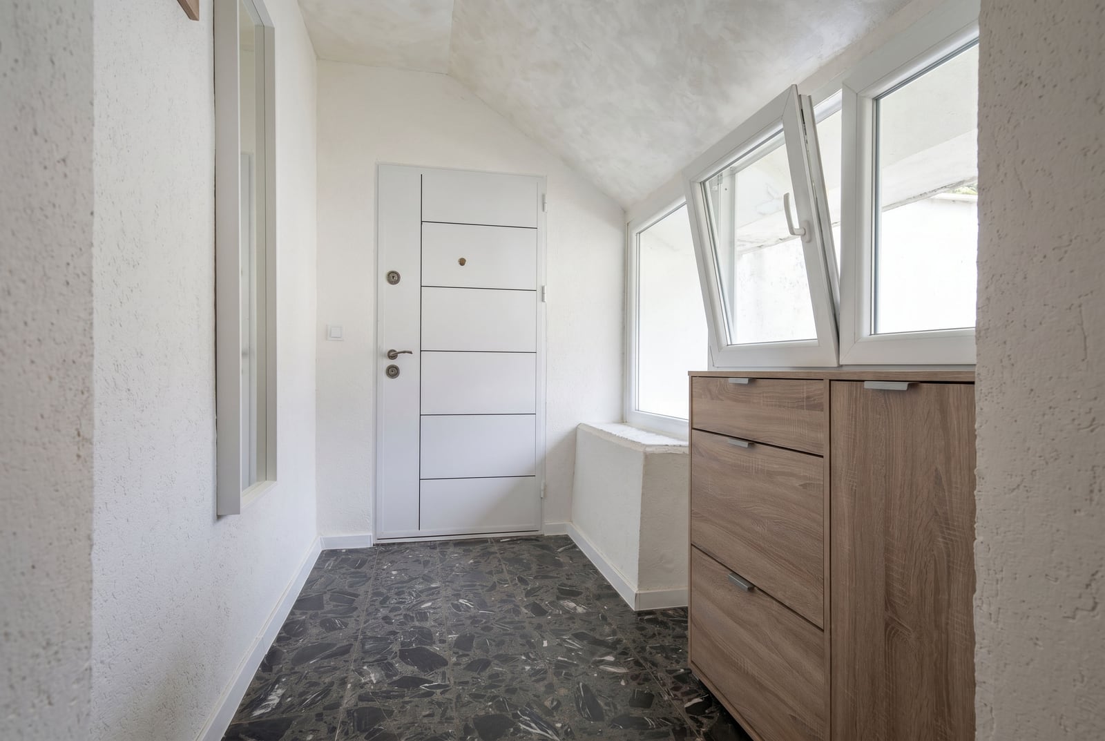 Bright hallway in an apartment in Budva, Montenegro: white door, wooden cabinet, panoramic windows, and stone flooring.