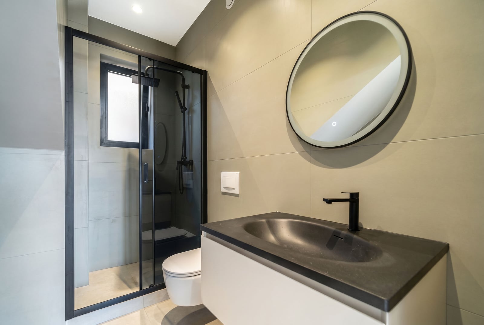 Kavač, Karadağ'daki bir şehir evinde modern banyo: duşakabin, siyah armatürler ve yuvarlak ayna.