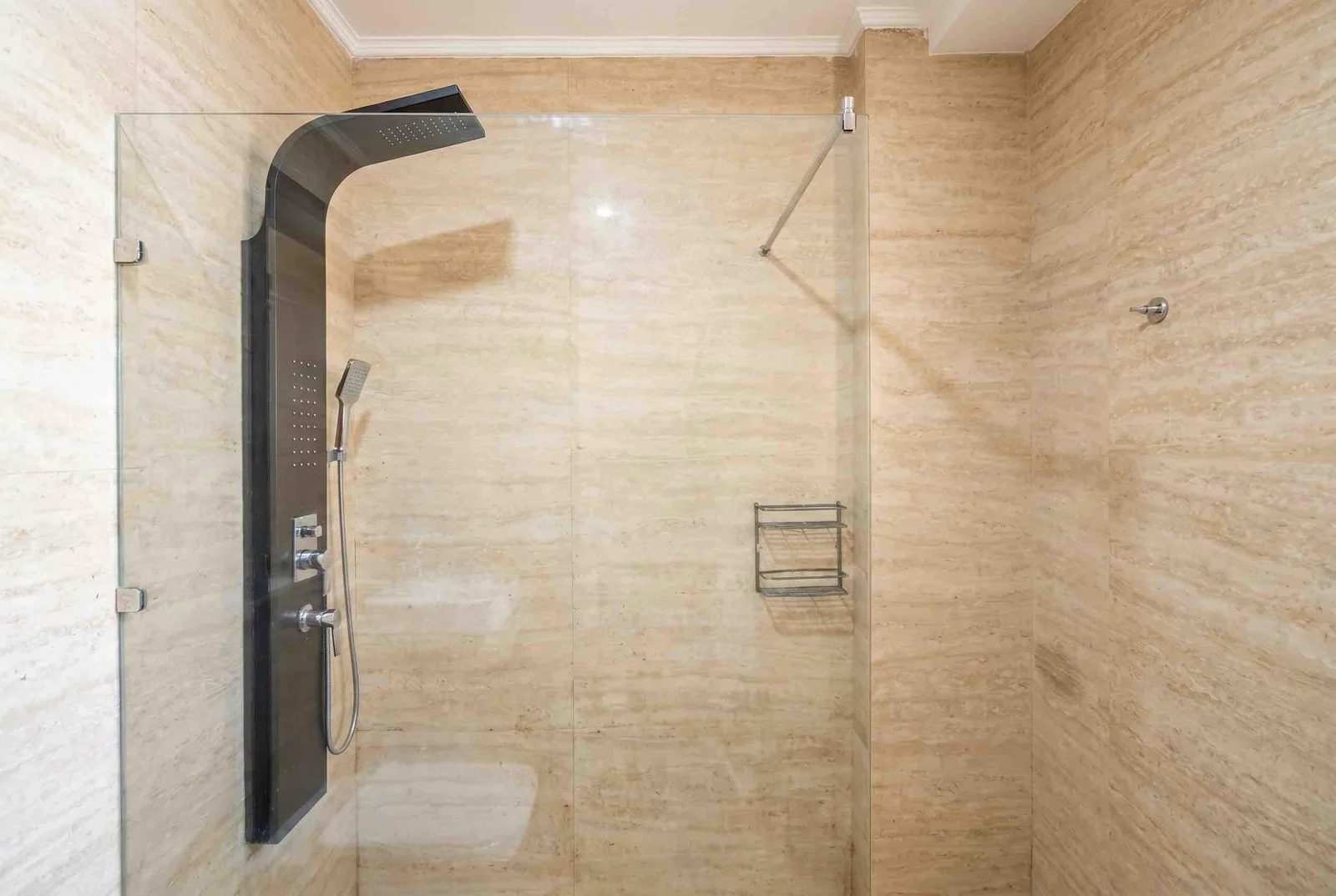 Shower enclosure with marble tiles and a black panel shower system behind a glass partition.