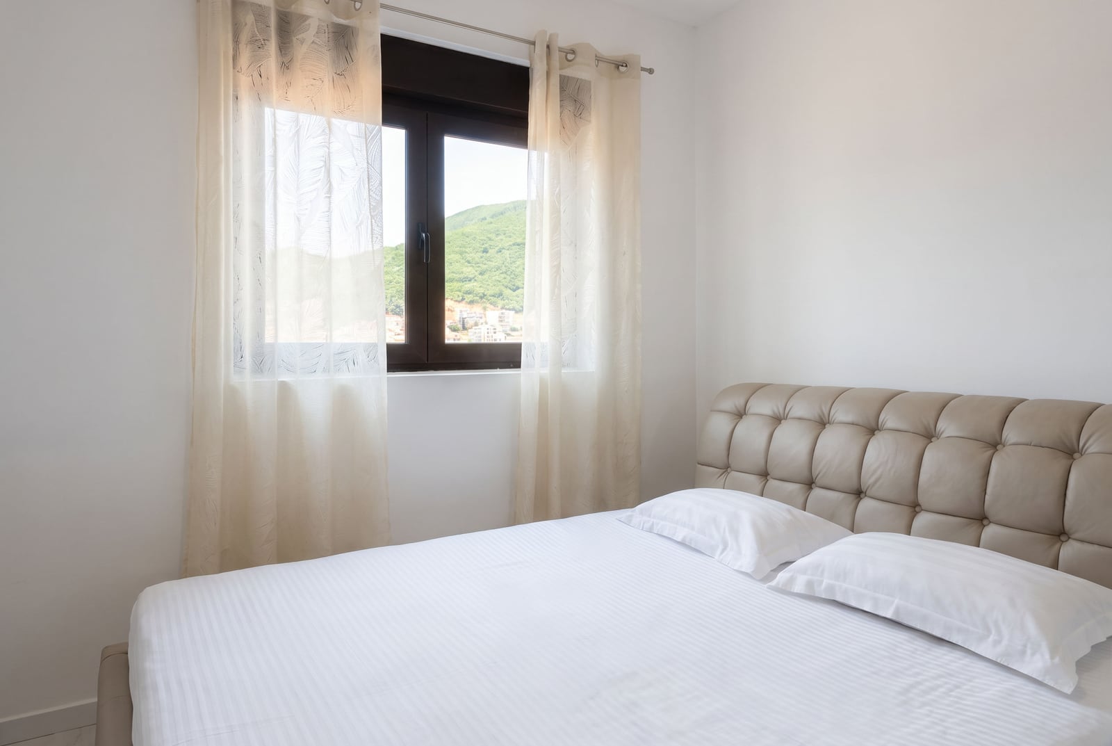 Bright bedroom with a soft beige headboard and mountain views in an apartment in Budva, Montenegro.