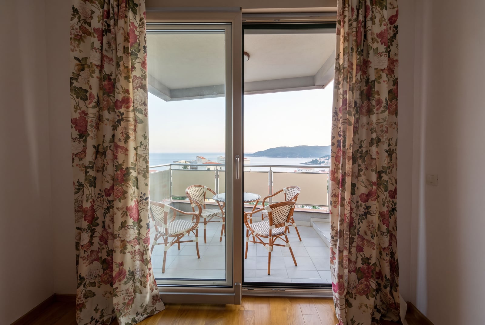 Exit to the balcony with wicker furniture and a sea view from the bedroom of an apartment in Bečići, Montenegro.