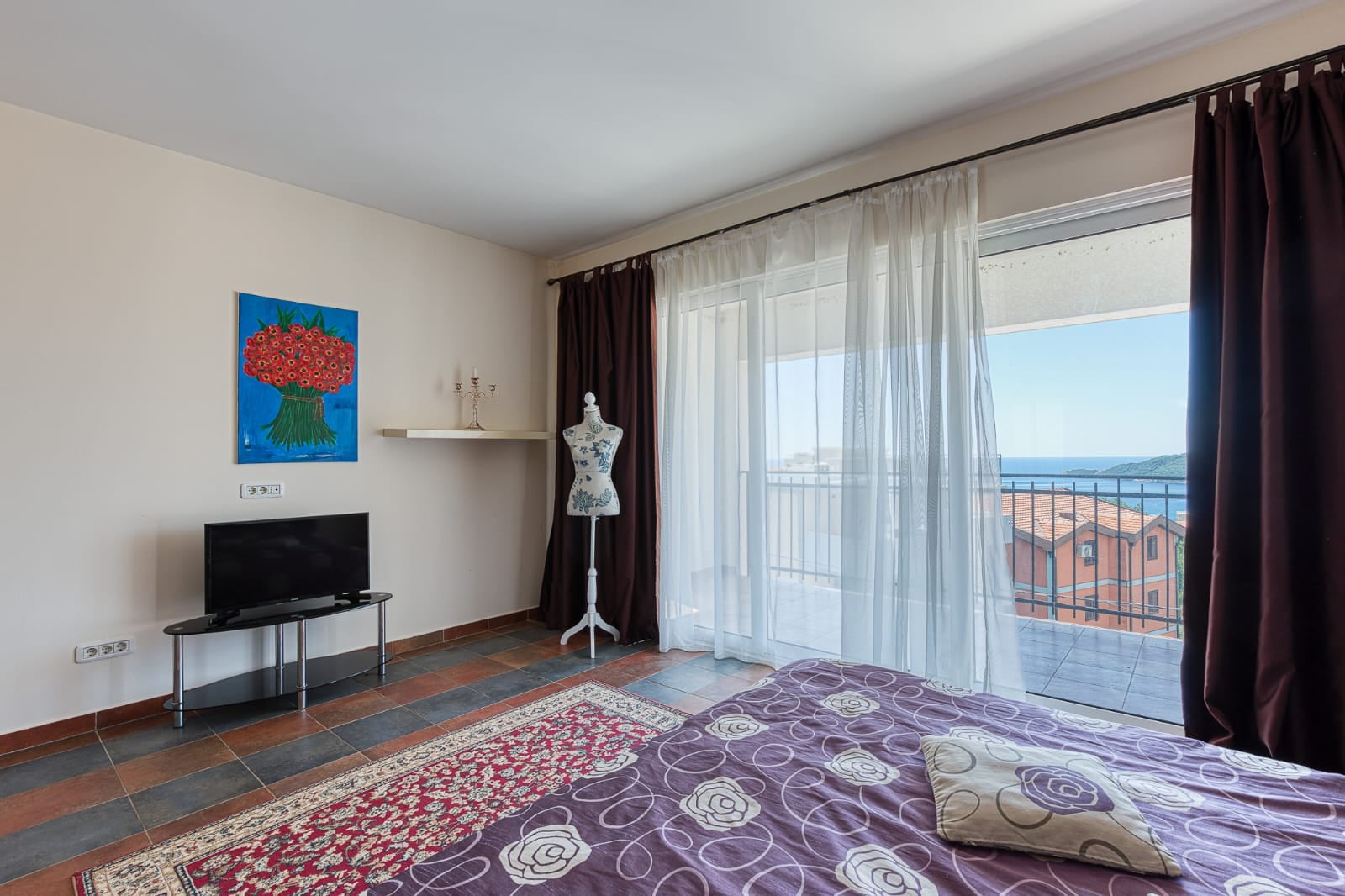 Chambre dans une villa à Bečići, Monténégro : lit, télévision, mannequin de couture et balcon panoramique avec vue sur la mer et les montagnes.