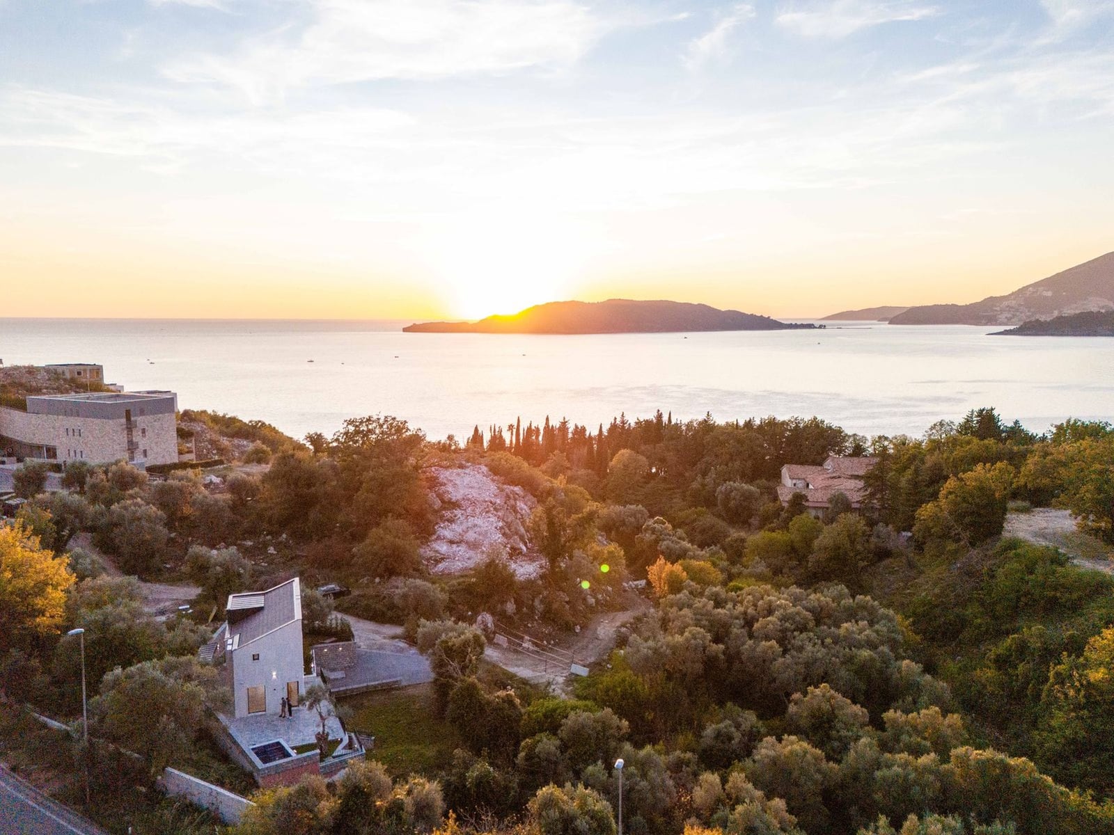 Villa moderne à Kamenovo, Monténégro, avec vue panoramique sur la mer et l'île au coucher du soleil, entourée de verdure.