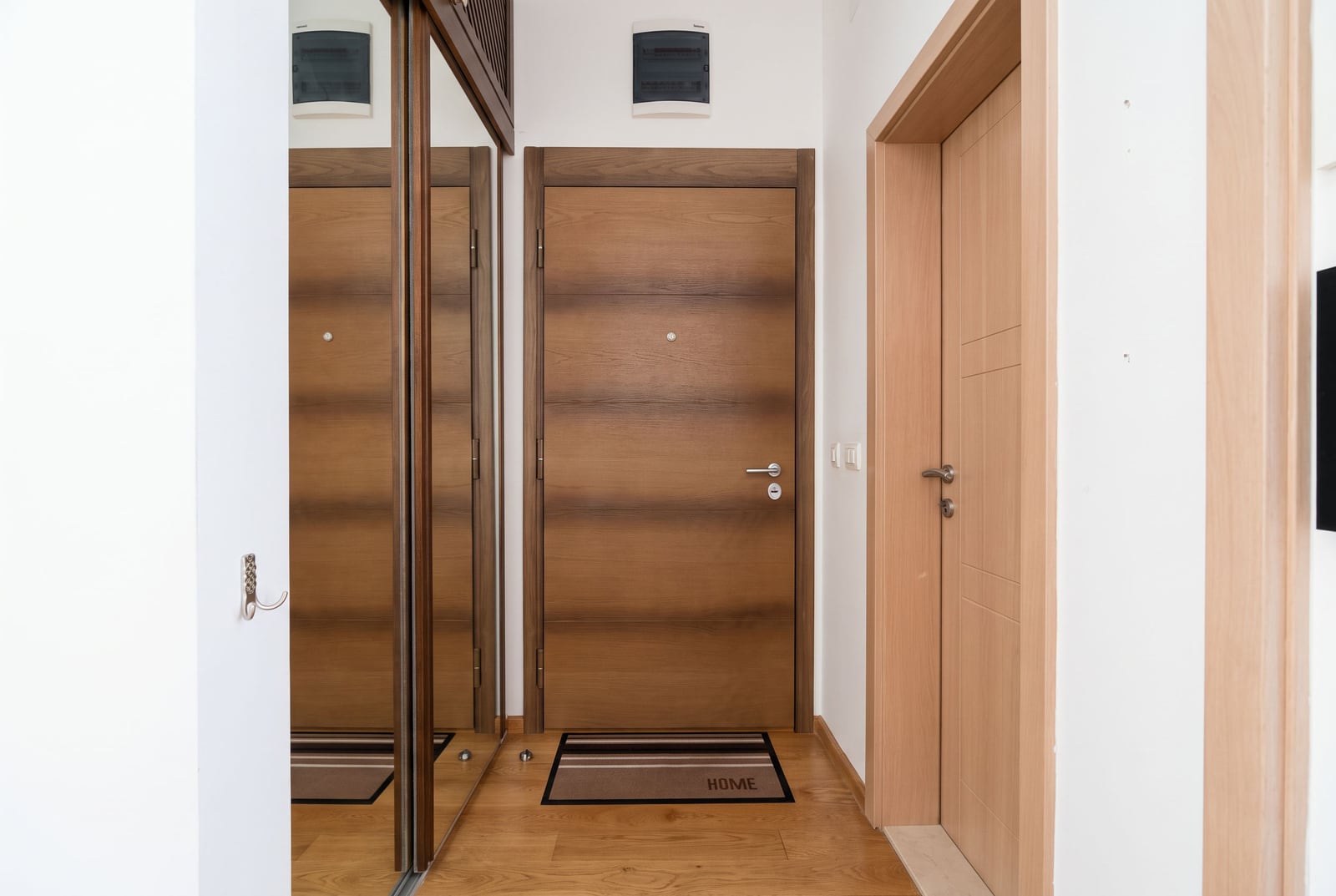 Modern hallway with a wooden entry door, sliding wardrobe, and laminate flooring in an apartment in Bečići, Montenegro.