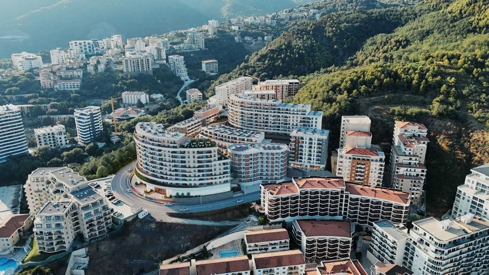 Karadağ, Bečići’deki konut kompleksinin havadan görünümü: dağlar ve yeşilliklerle çevrili modern çok katlı binalar.