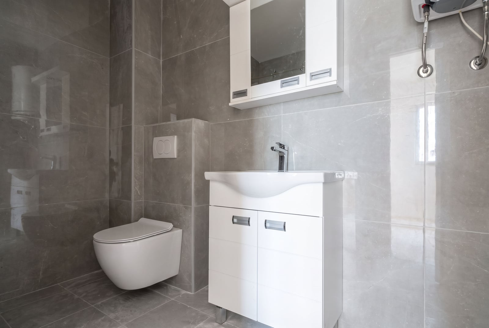 Modern bathroom in an apartment in Bar, Montenegro: gray tiles, wall-hung toilet, and a white vanity with a sink.