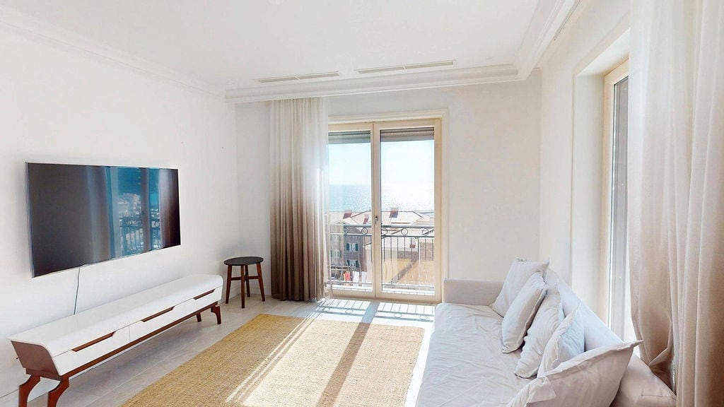 Svetla dnevna soba u stanu u Luštici, Crna Gora: moderan nameštaj, TV, panoramski prozori sa pogledom na more.