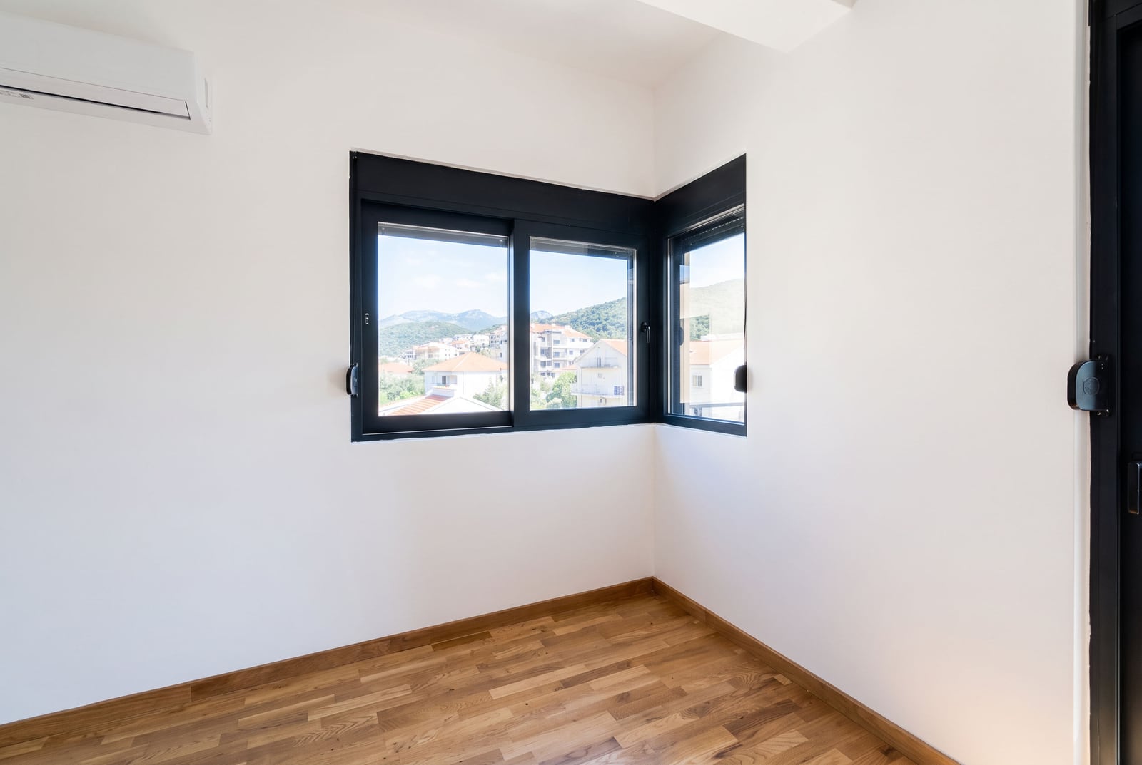 Bright bedroom with parquet flooring and a corner window in a new apartment in the city of Bar, Montenegro, with a view of the mountains and the city.