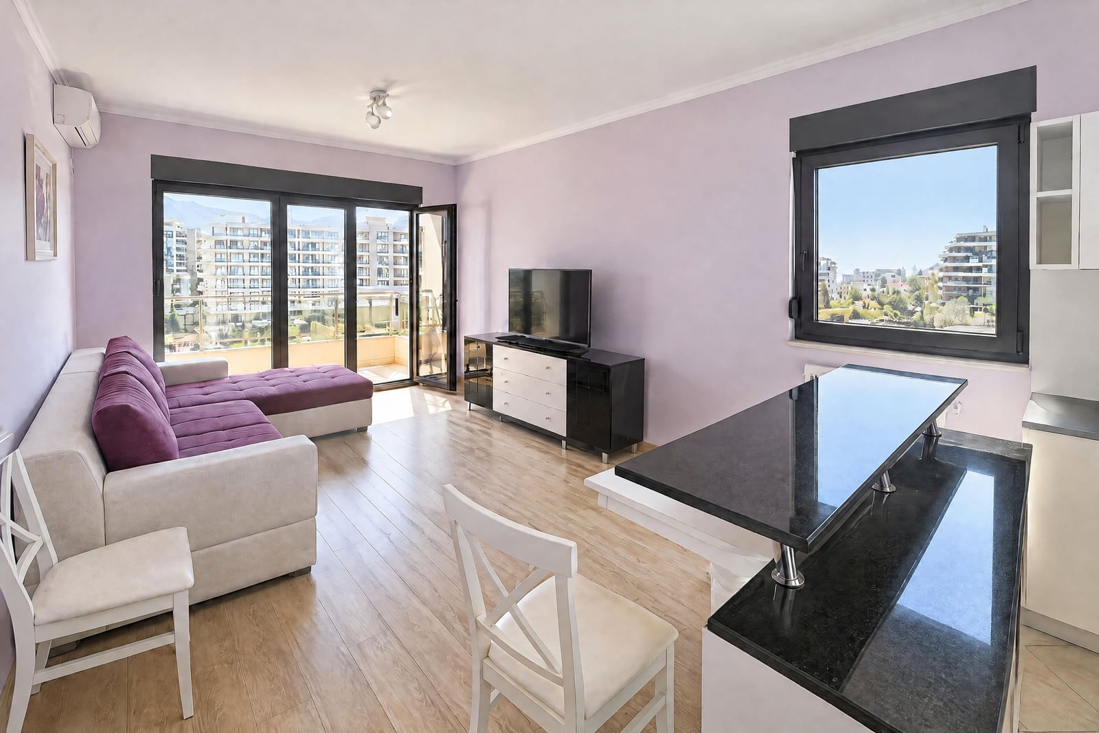 Spacious living room with a purple sofa, dining area, and panoramic windows in an apartment in Budva, Montenegro