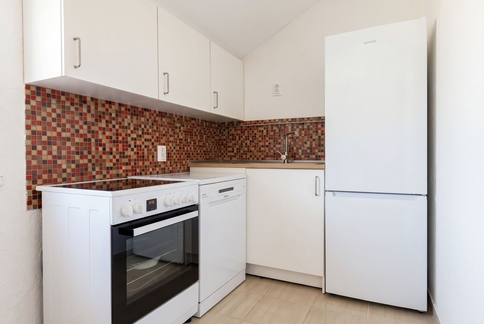 Bright kitchen in a Budva apartment, Montenegro: white cabinetry, stove, dishwasher, and mosaic backsplash.