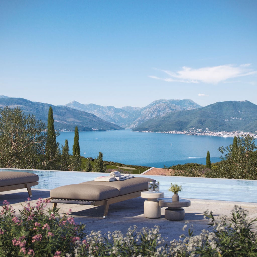 Infinity pool with a view of the Bay of Kotor and mountains in the Luštica residential complex, Montenegro, with a lounge area and sun loungers.