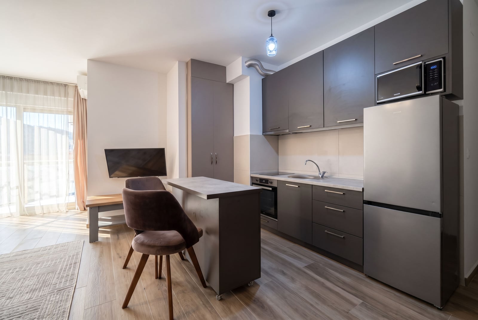 Moderna kuhinja u stanu u Budvi, Crna Gora: sivi nameštaj, barska stolica, kućni aparati i izlaz na balkon