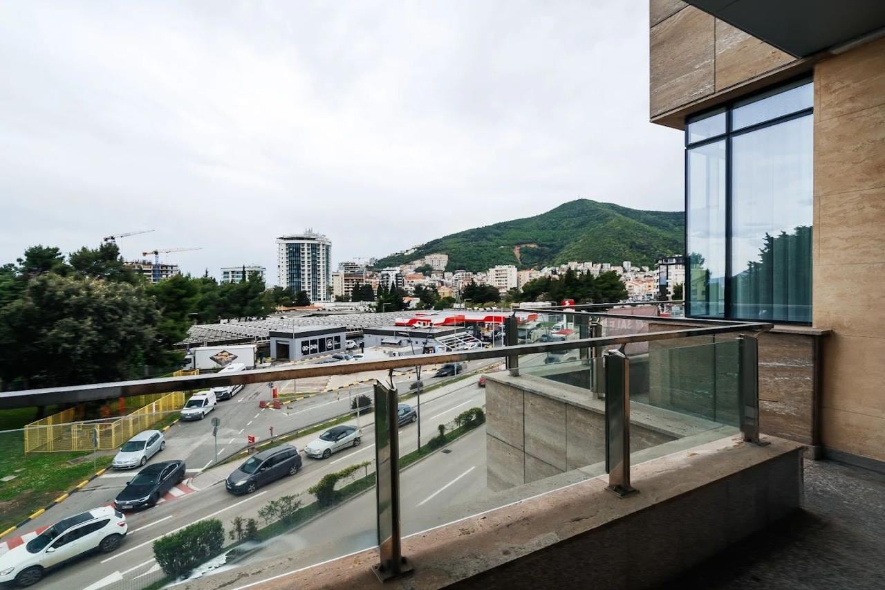Pogled s balkona moderne stana u Budvi, Crna Gora: panorama grada, planine i gradska infrastruktura.