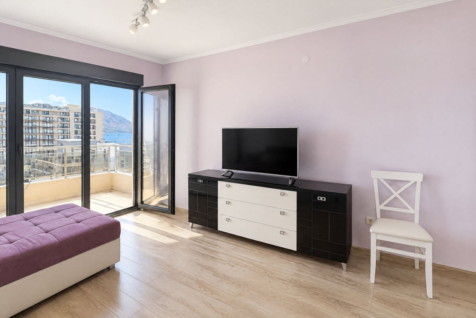 Bright bedroom with furniture, TV, and panoramic balcony access with sea view in Budva, Montenegro