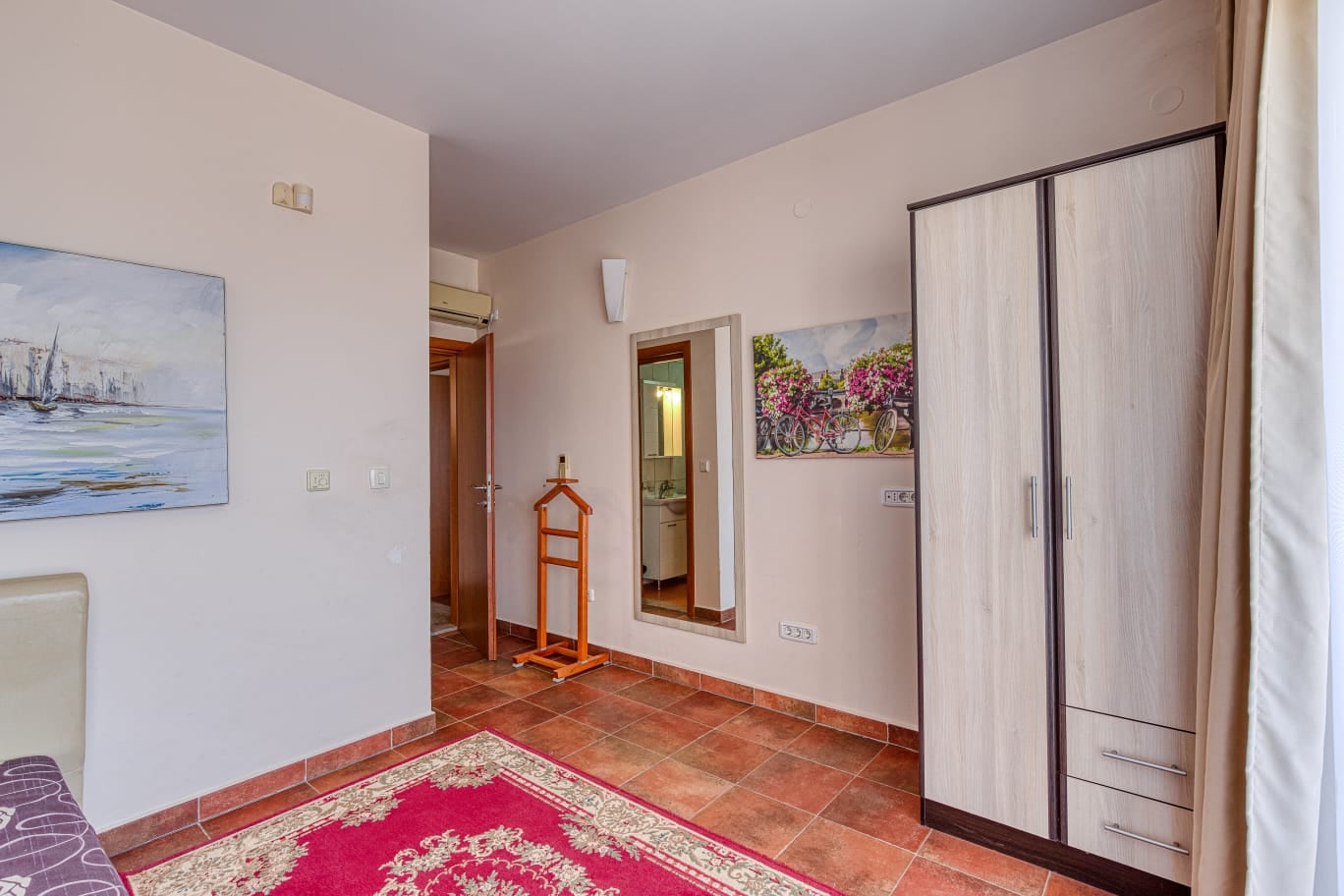Chambre dans une villa à Bečići, Monténégro : pièce lumineuse avec carrelage, armoire, miroir et décoration murale.