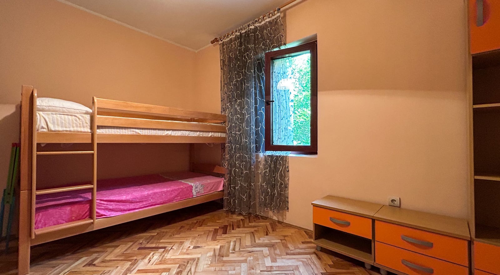 Kinderzimmer mit Etagenbett in einer Villa, Stadt Dobrota, Montenegro: Parkettboden, orangefarbene Möbel und Blick in den Garten.