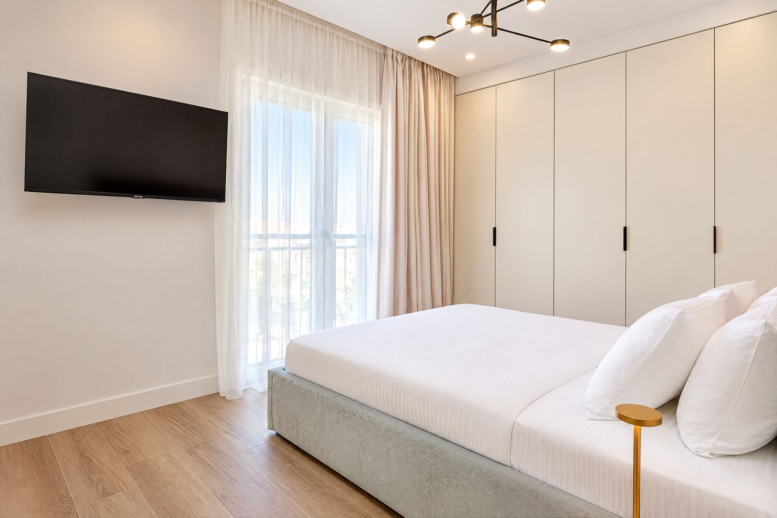 Modernes Schlafzimmer mit weißem Bett, Schrank, TV und Balkon in einer Wohnung in Luštica, Montenegro