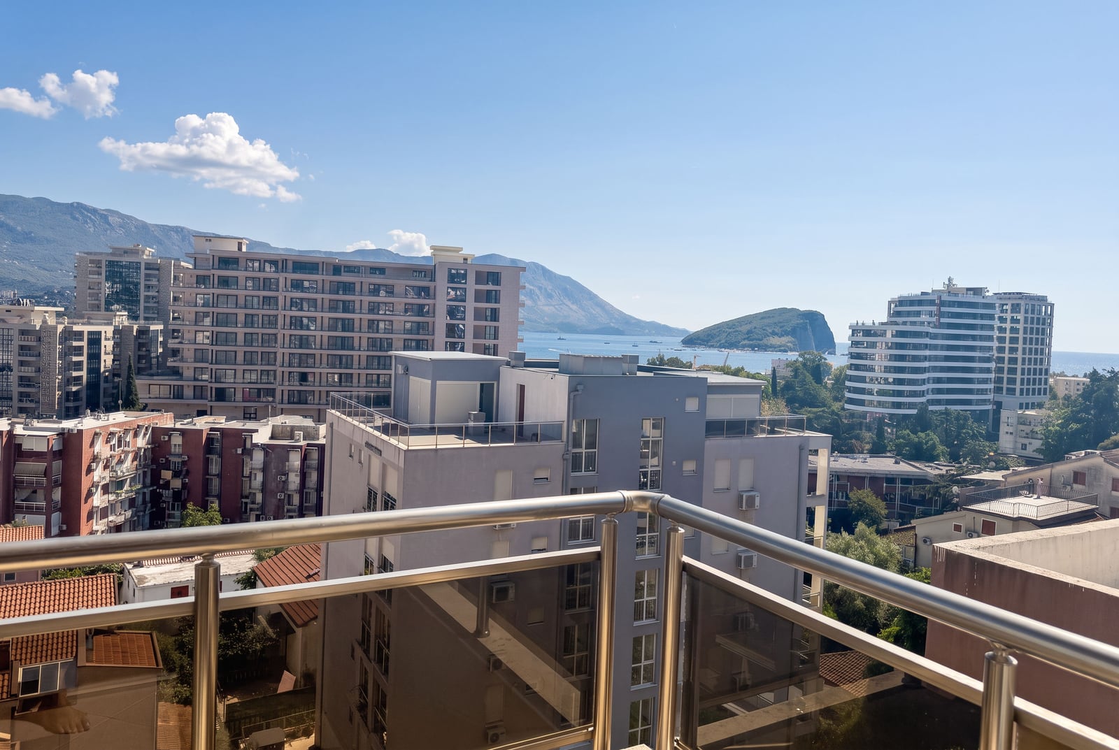 Panoramic view from the balcony of an apartment in Budva, Montenegro: city buildings, mountains, and the sea.