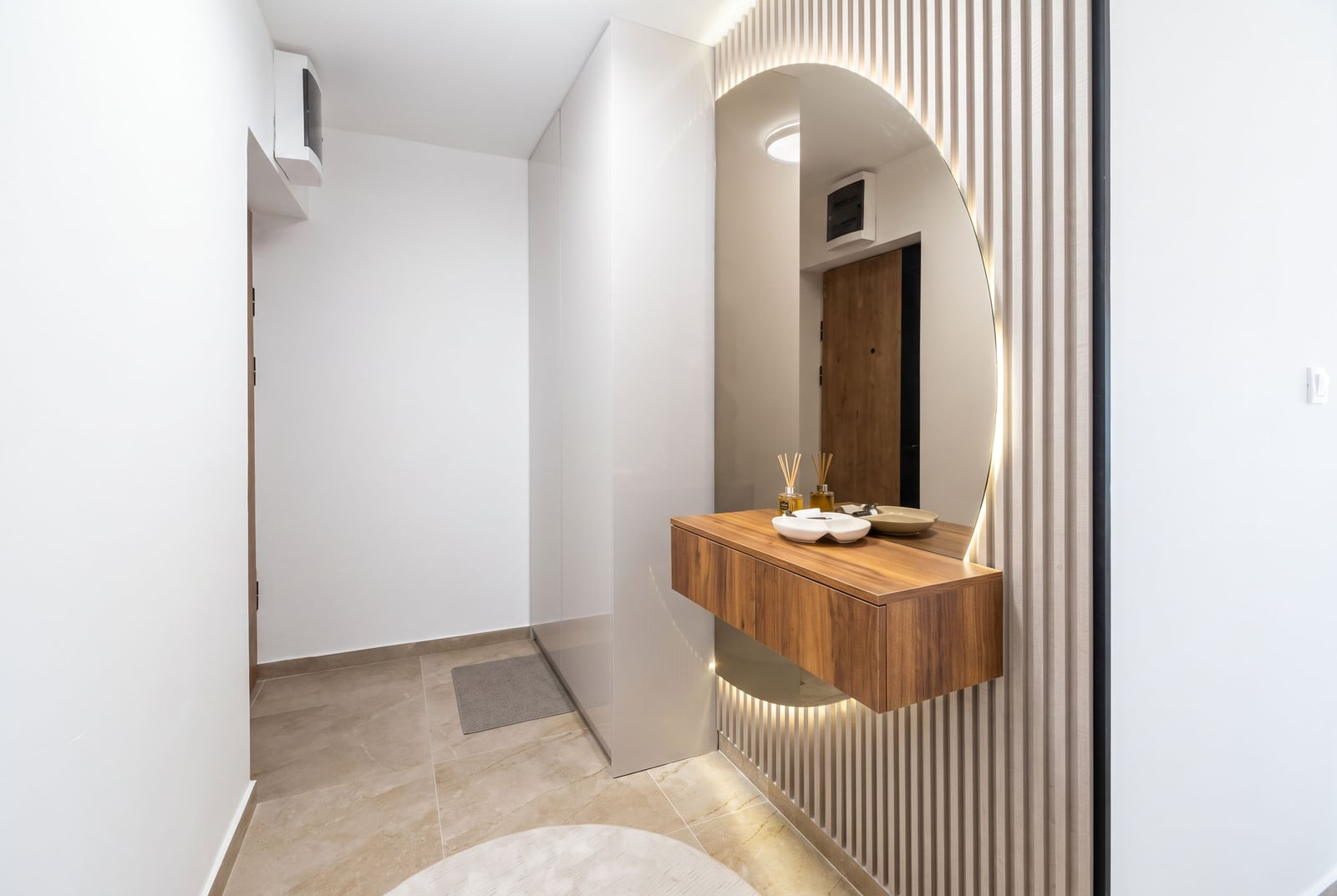 Modern hallway in an apartment in Budva, Montenegro: wall-mounted wooden cabinet, round mirror with lighting, and slatted pa...