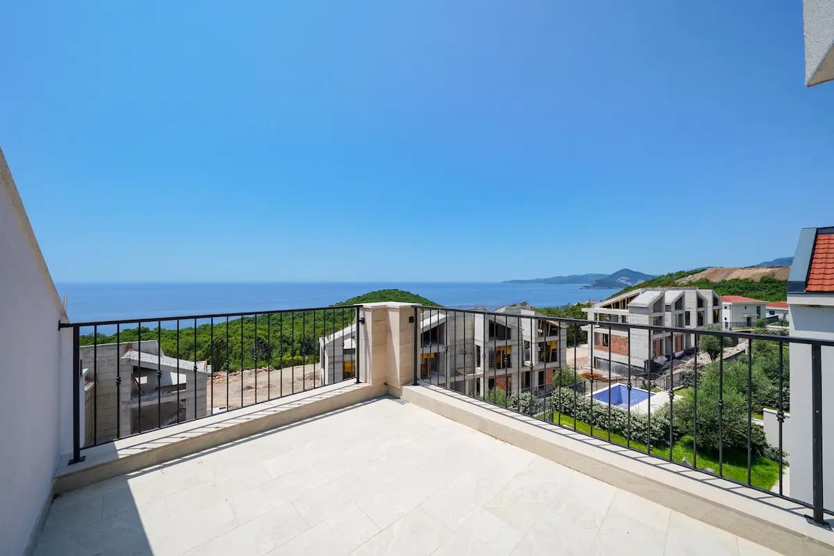 Terrasse ouverte d'une villa à Reževići, au Monténégro, avec vue panoramique sur la mer, les montagnes et un complexe résidentiel en construction.