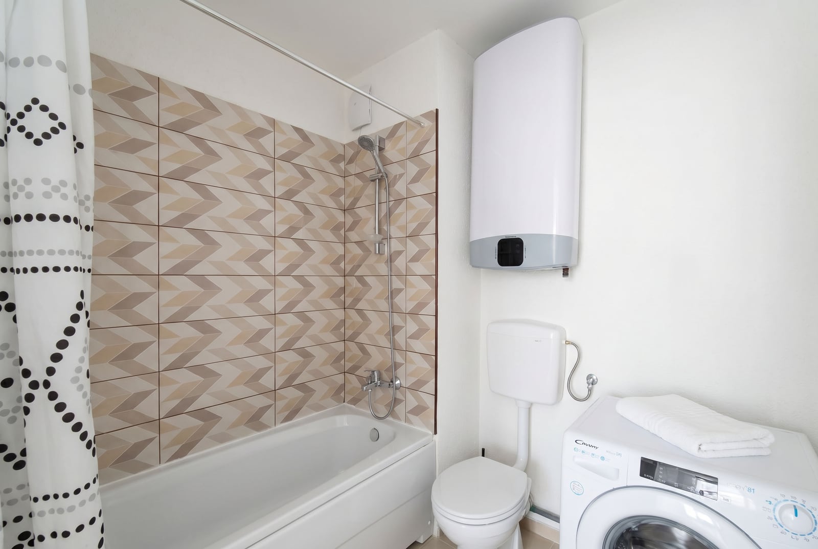 Bathroom in a Budva apartment, Montenegro: geometric patterned tiles, bathtub, water heater, and washing machine.