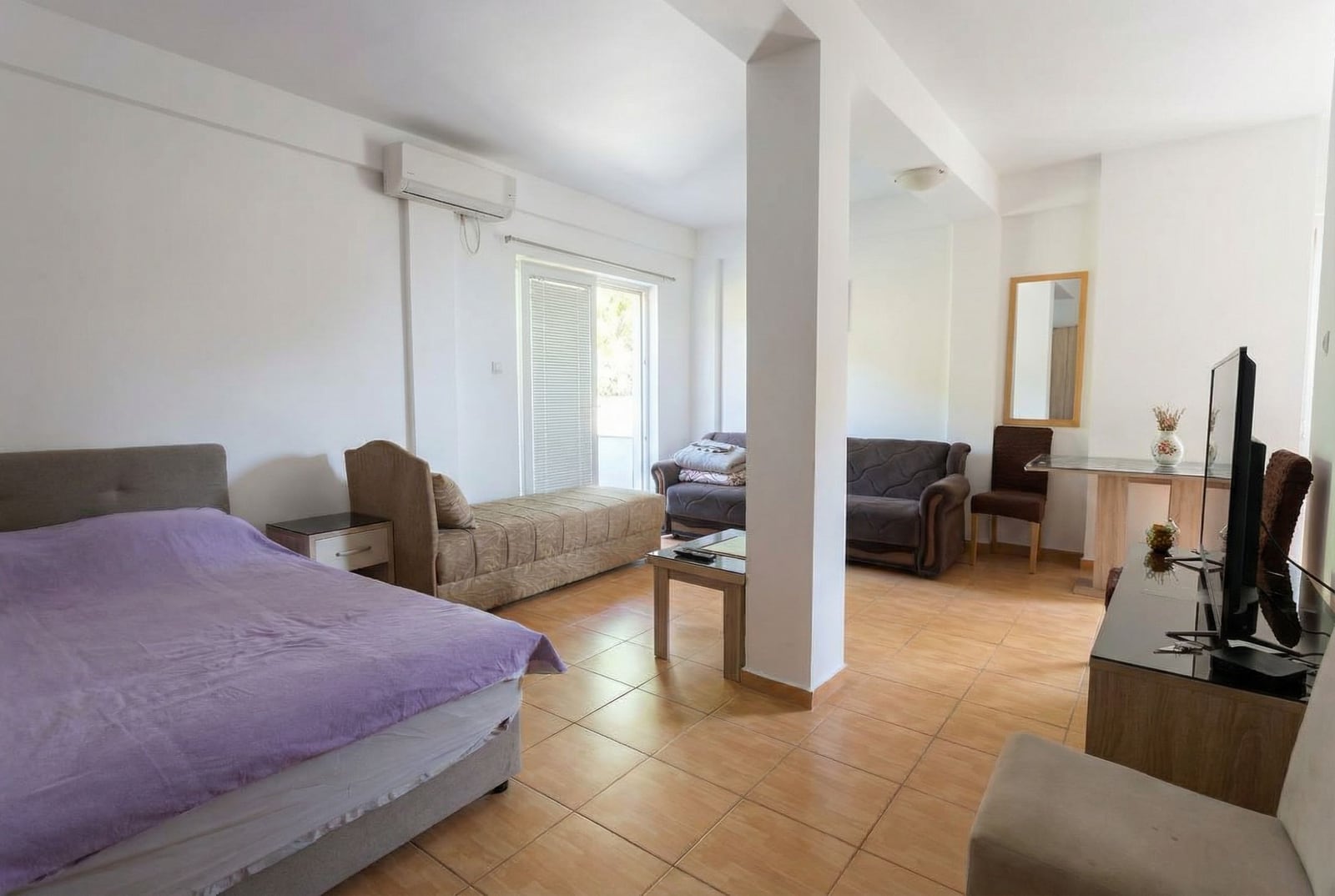 Osvetljen studio u Budvi, Crna Gora: dnevna soba sa bračnim krevetom, sofom, TV zonom i izlazom na balkon.
