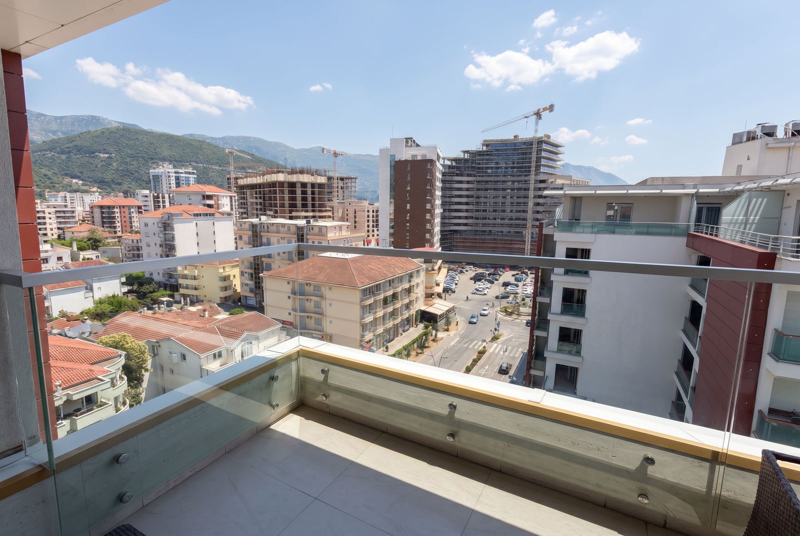 View from the balcony of an apartment in Budva, Montenegro: panoramic view of the city, modern buildings, and mountains in the background.