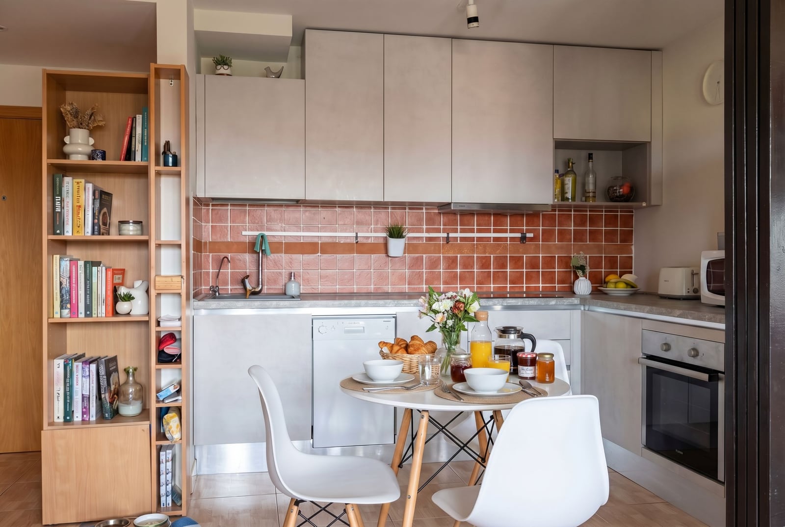 Modern kitchen in an apartment in Budva, Montenegro: light-colored cabinets, terracotta backsplash, and a dining area with a table.