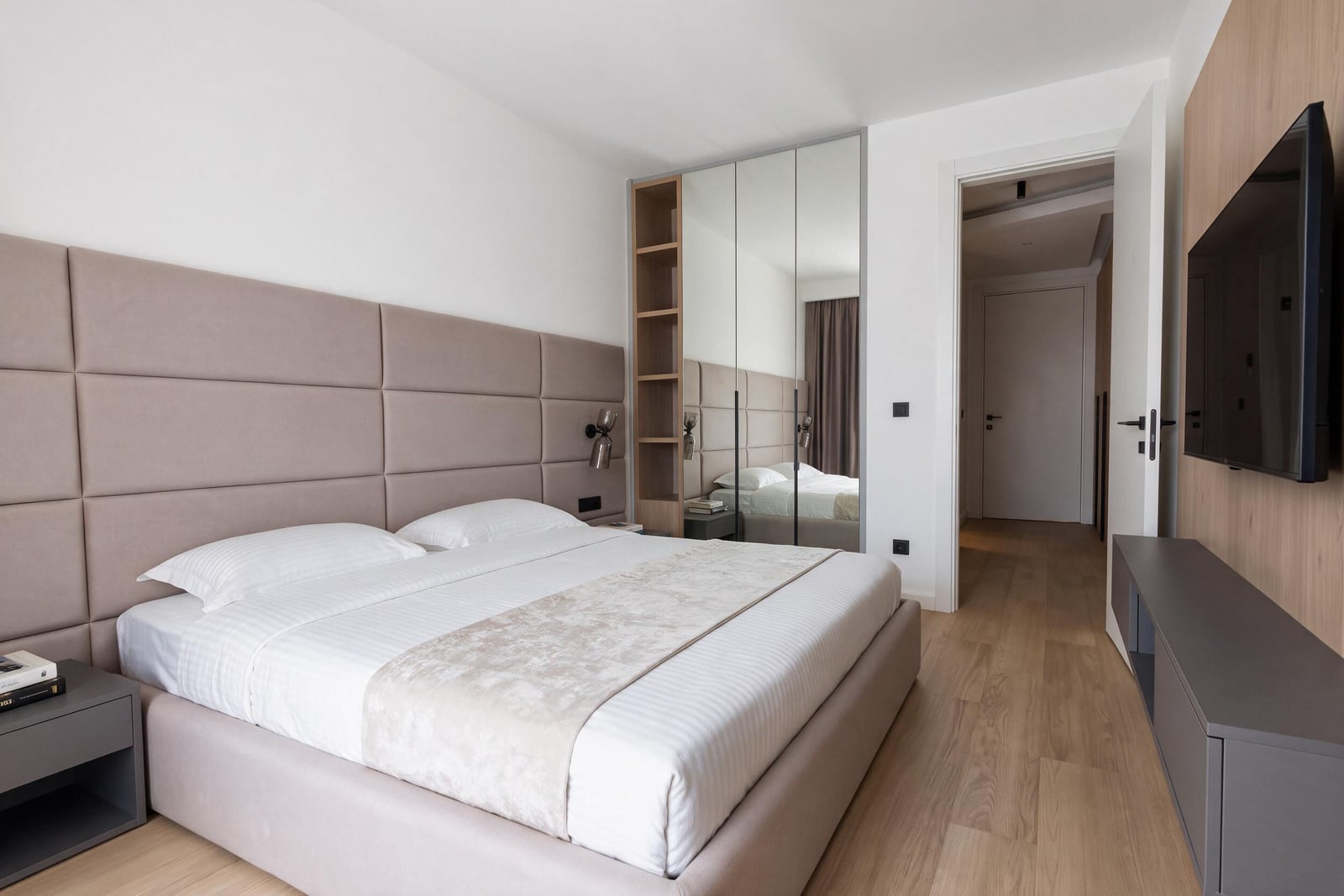 Modern bedroom with an upholstered bed headboard, mirrored wardrobe, and TV in an apartment in Budva, Montenegro.