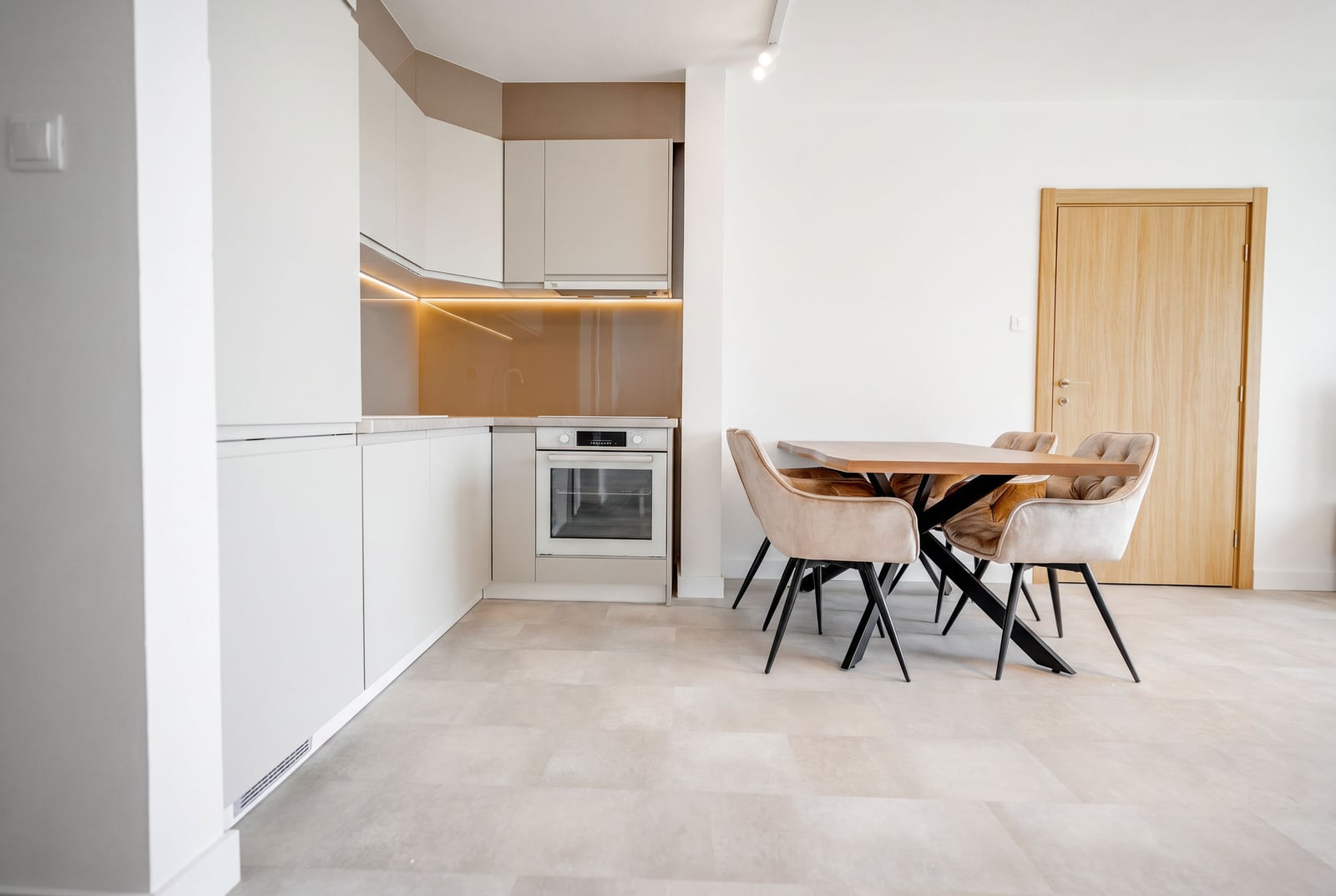 Modern kitchen-dining area in an apartment, Sveti Stefan, Montenegro: light-colored kitchen unit, dining table, and upholstered chairs.