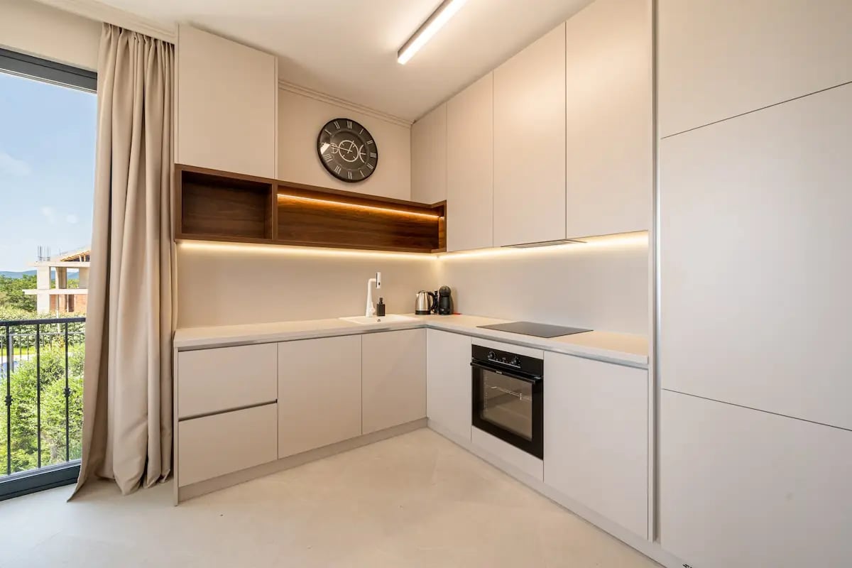 Modern bright kitchen in a villa in Rezevici, Montenegro: built-in appliances, ambient lighting, and balcony access.