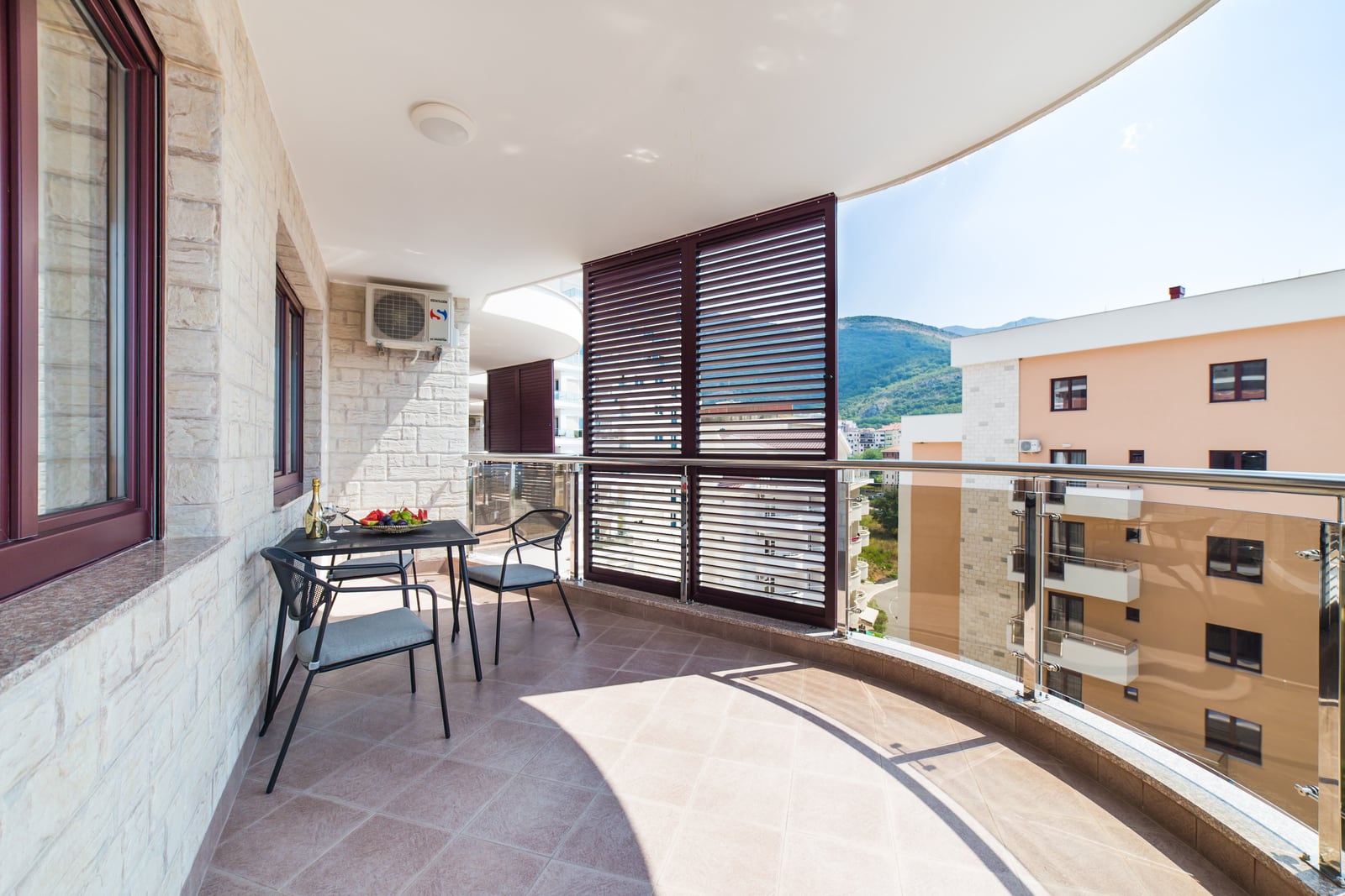Geräumiger Balkon mit Möbeln und Bergblick in einer Wohnung in Bečići, Montenegro: Steinverkleidung und Glasgeländer.