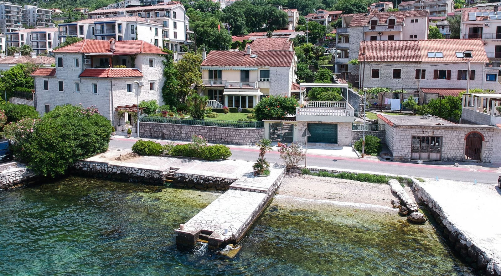 Villa in Dobrota, Montenegro: Blick auf das Haus mit Terrasse, privatem Steg und Zugang zum Meer, umgeben von Grün.