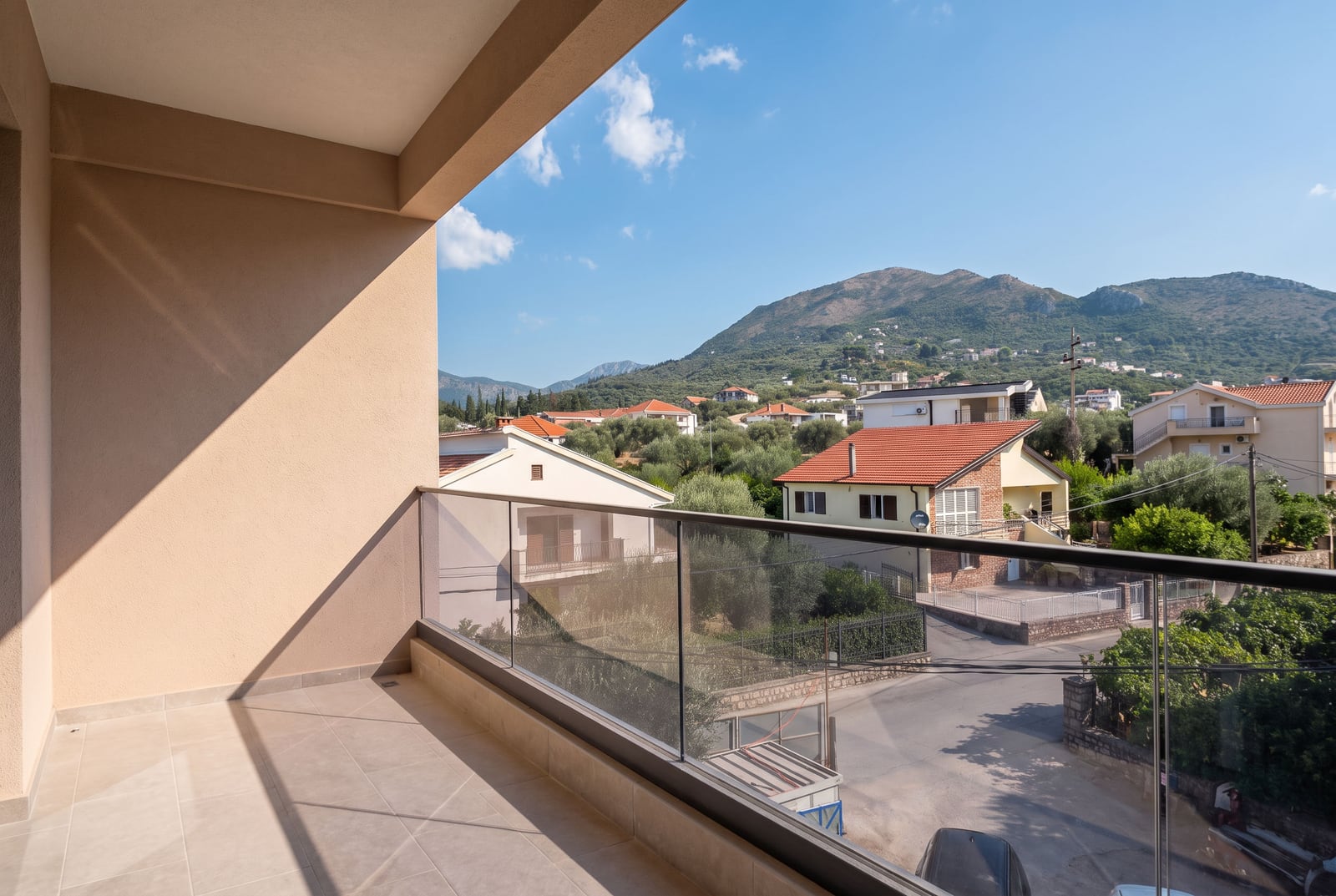 View from the balcony of a modern apartment in the city of Bar, Montenegro: glass railing, tile flooring, and a panoramic view of the mountains.