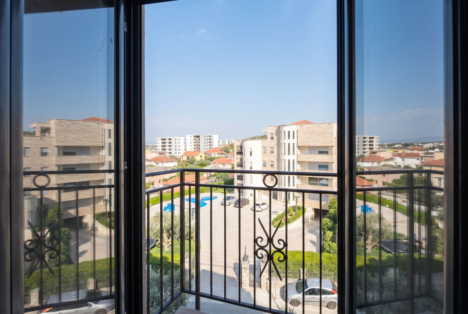 View from the balcony of an apartment in the city of Bar, Montenegro: panorama of a residential complex with a swimming pool and parking.