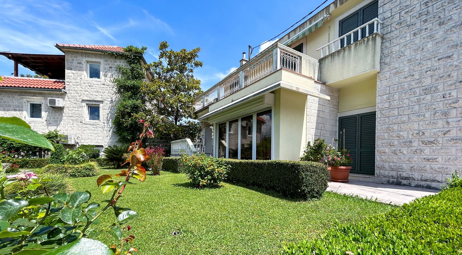 Zweistöckige Steinvilla mit Terrasse und gepflegtem Garten in Dobrota, Montenegro: Außenansicht des Hauses mit grünem Rasen.