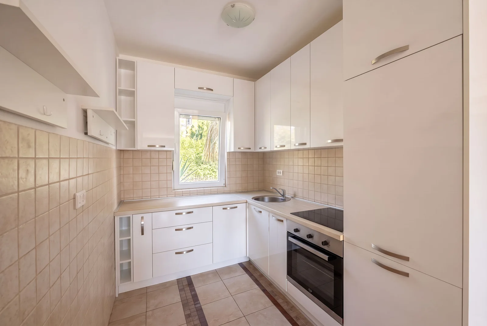 Кухня с белыми шкафами, плитой, раковиной и бежевой tiled стеной.