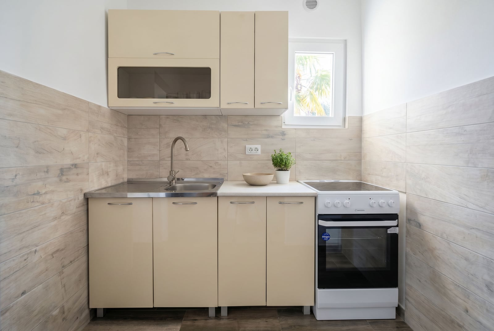 Cuisine compacte dans une maison, Krašići, Monténégro : meubles beiges, cuisinière, évier et revêtement en carrelage imitation bois.