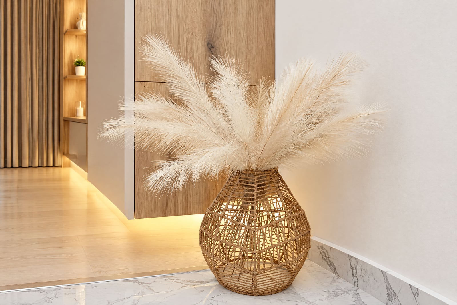 Woven rattan lamp vase with dried pampas grass on a marble floor in a modern hallway.