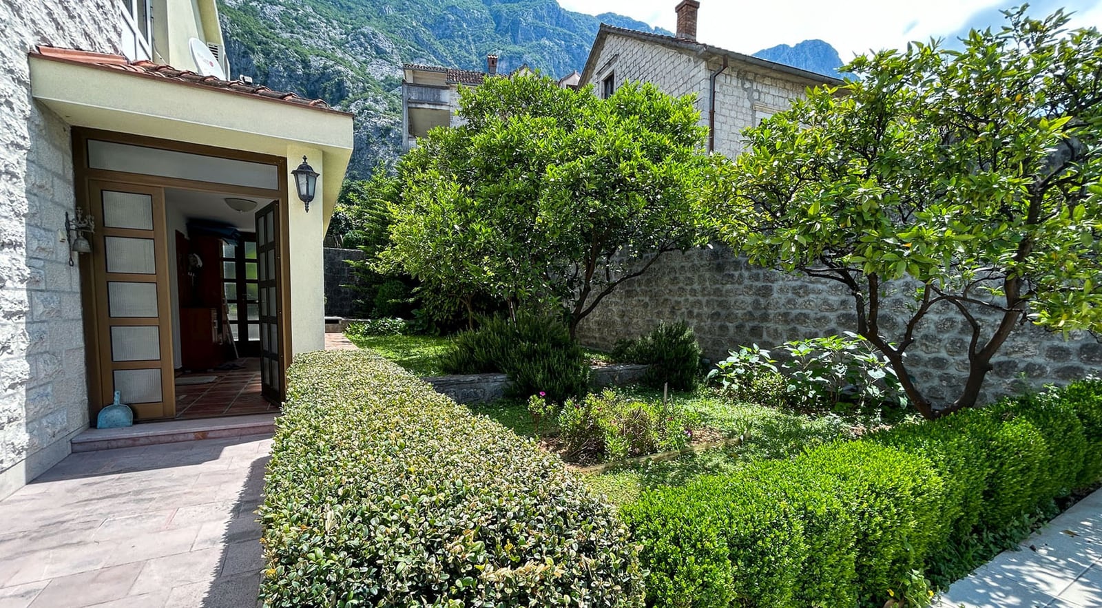 Gemütlicher grüner Garten und Terrasse einer Steinvilla in Dobrota, Montenegro, mit Blick auf die Berge und Landschaftsgestaltung.