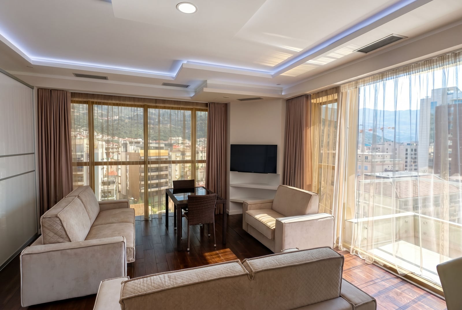 Modern living room in a Budva apartment, Montenegro: light-colored furniture, panoramic windows with views of the city and mountains.
