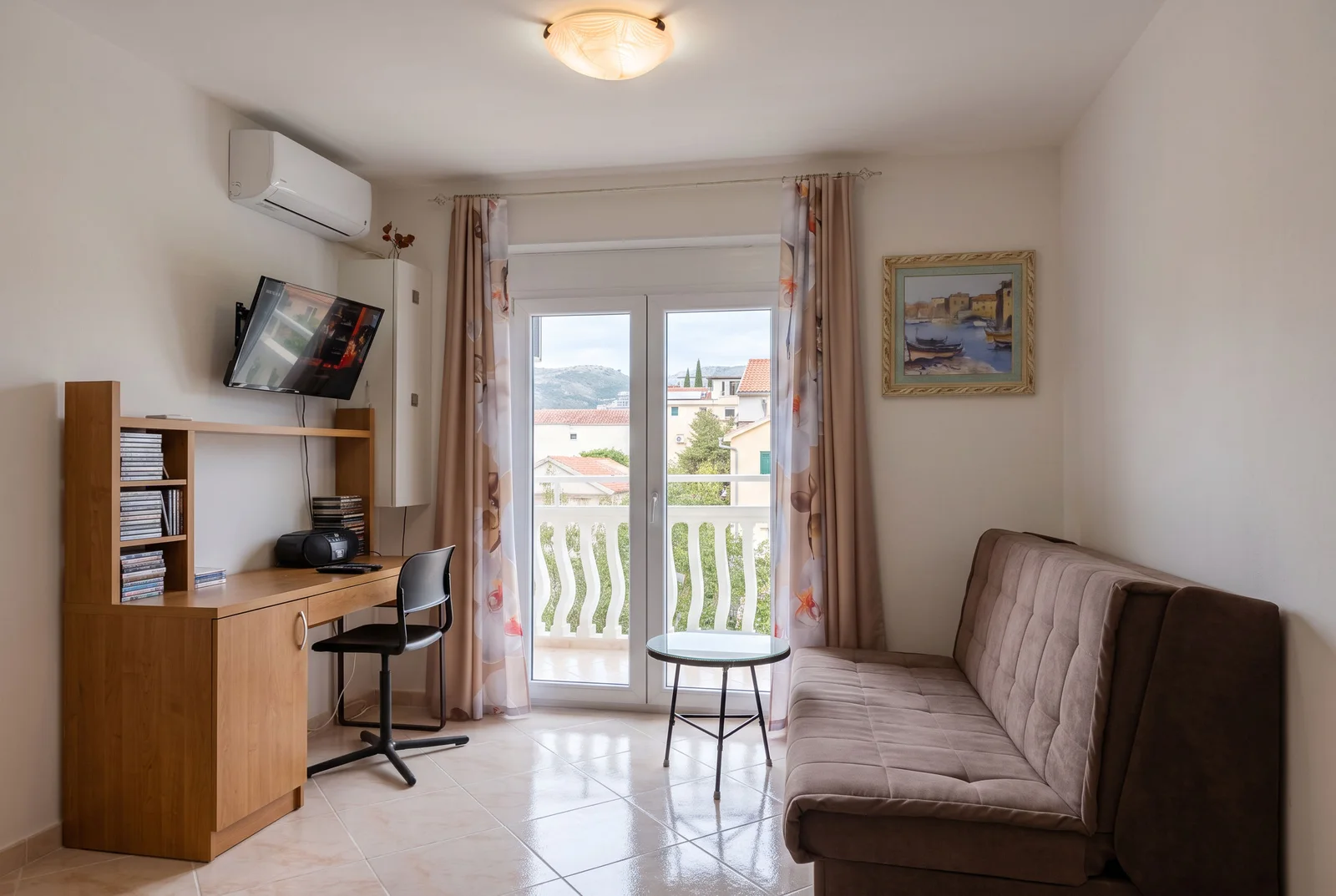 Living room with a sofa, wooden desk, TV, and glass door leading to a balcony.