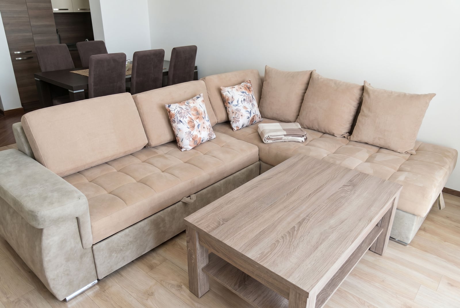 Living room in a Budva apartment, Montenegro: beige sectional sofa, wooden coffee table, and dining area.
