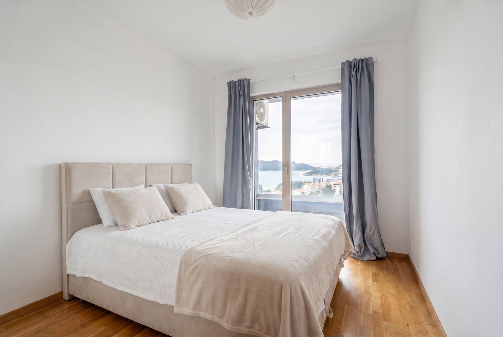 Bright bedroom with a double bed and a sea view in an apartment, Becici, Montenegro. Parquet flooring and a panoramic window.