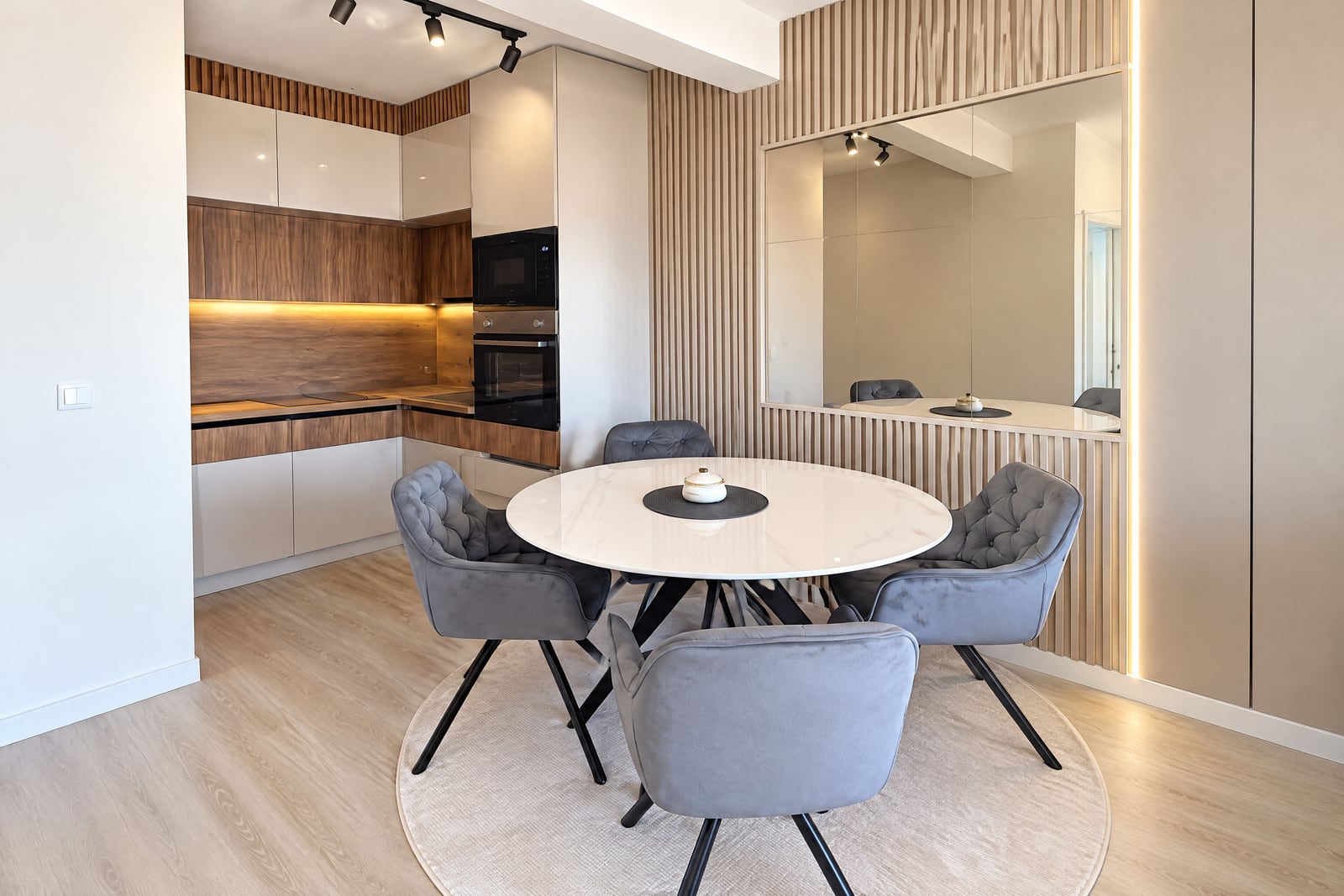 Modern kitchen in an apartment in Budva, Montenegro: dining area with a round table, gray armchairs, wooden panels and built-in...