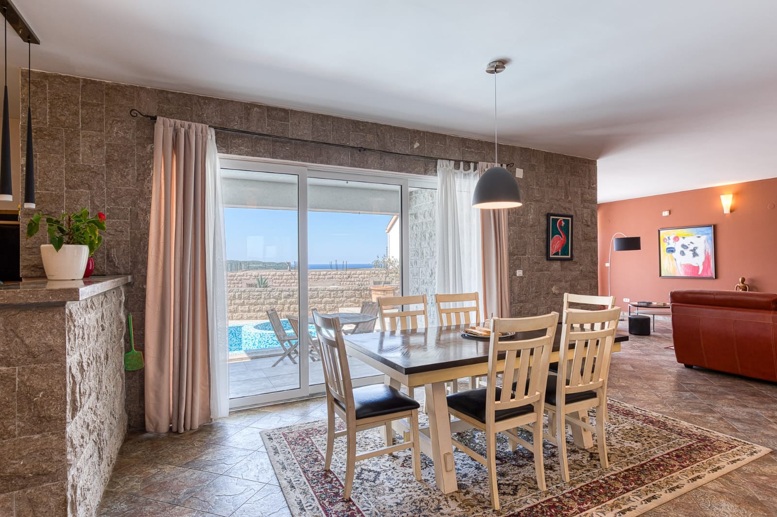 Salon avec coin repas dans une villa à Bečići, Monténégro : finitions en pierre, accès à la piscine et vue sur la mer.