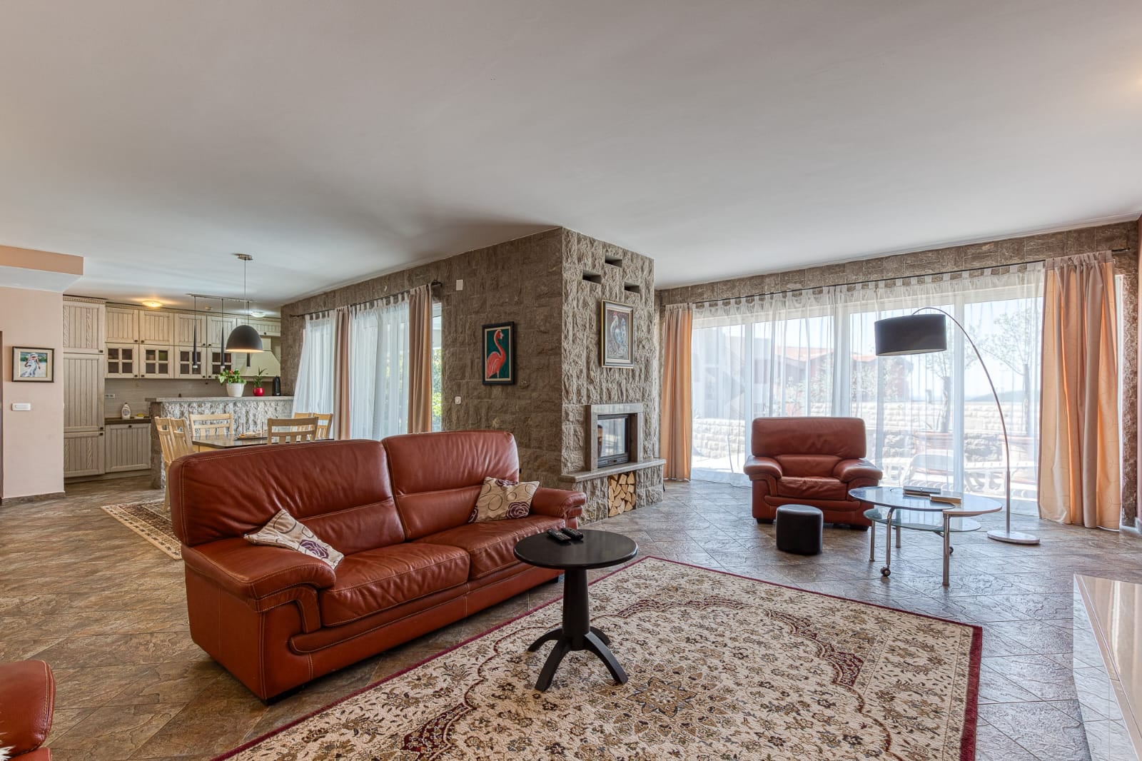 Salon avec cheminée en pierre et mobilier en cuir dans une villa à Bečići, Monténégro. Aménagement à aire ouverte avec cuisine et terrasse.