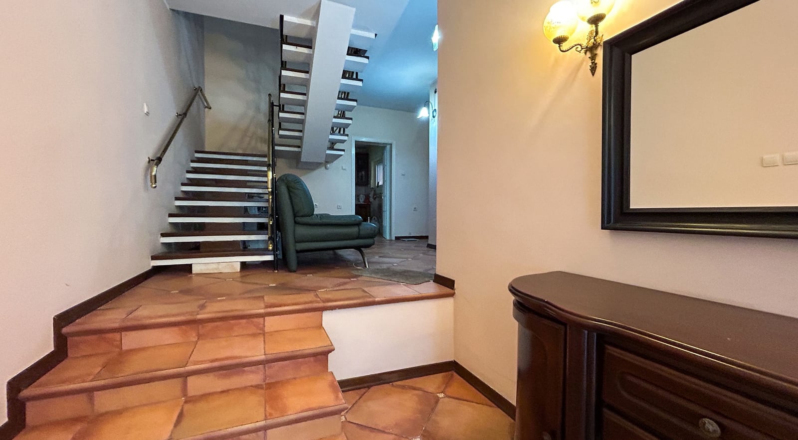 Innenraum einer Villa in Dobrota, Montenegro: Eingangsbereich mit Treppe, Fliesenboden, Kommode und Sessel im Wohnzimmer.