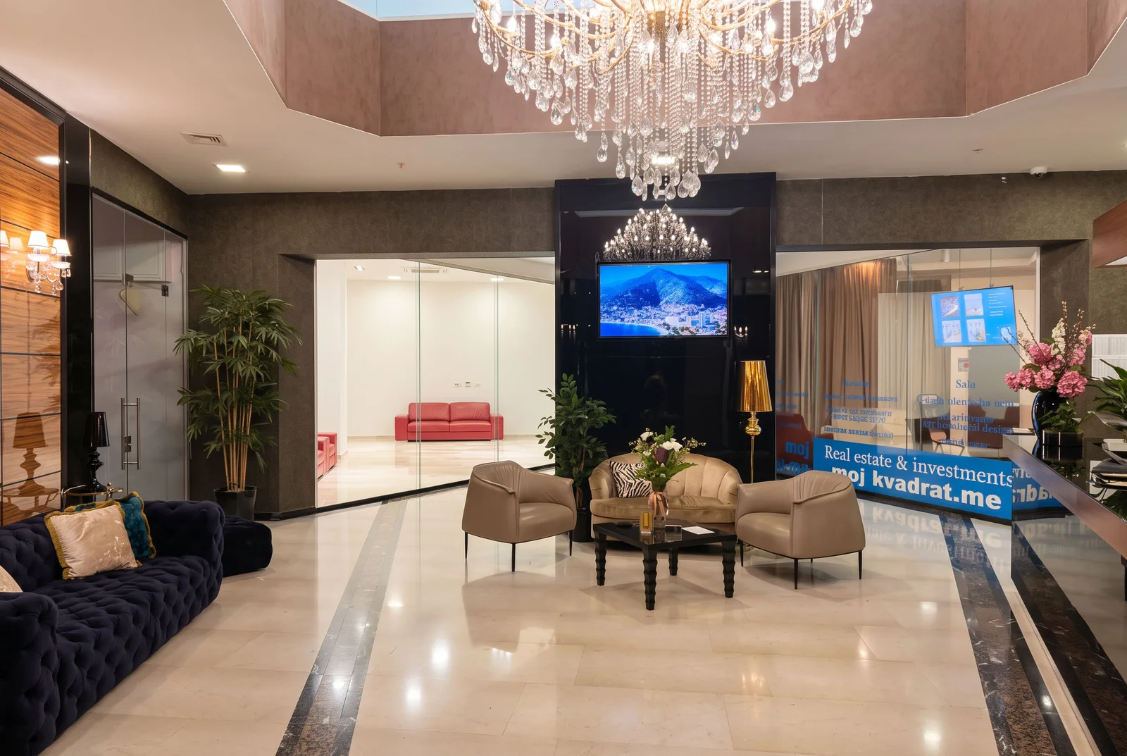 Luxury interior featuring a crystal chandelier, seating area, and real estate reception desk on marble floors.