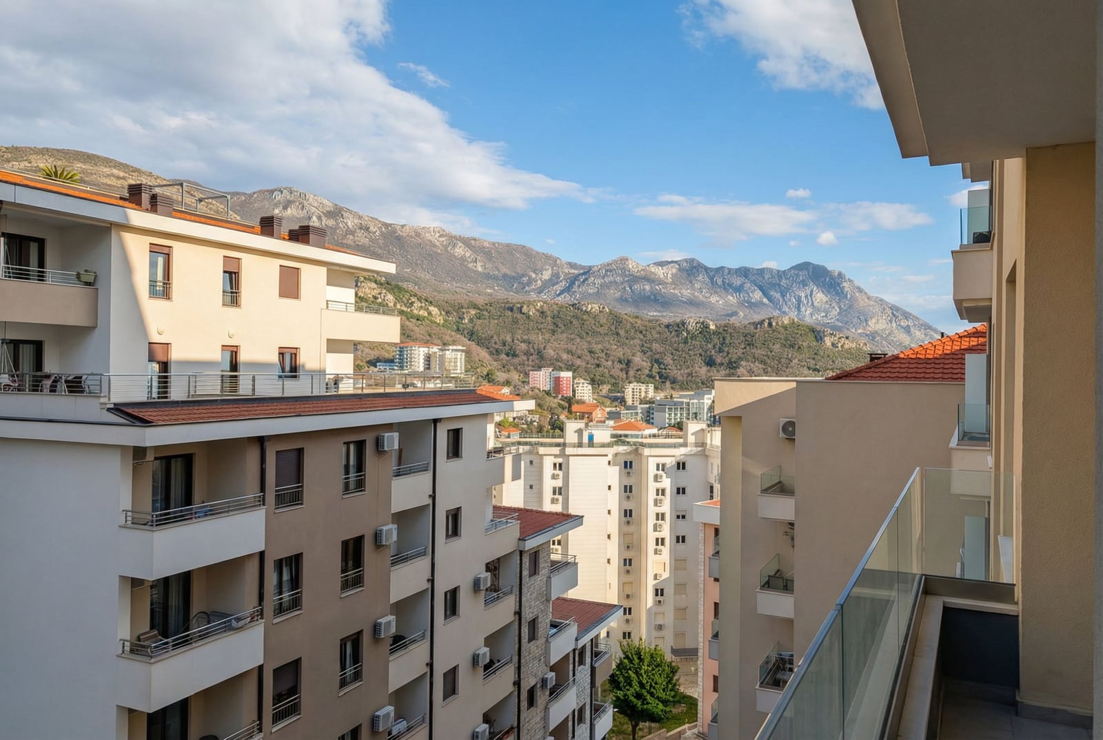 Pogled sa balkona stana u Bečićima, Crna Gora: moderne stambene zgrade i panoramski pejzaž planinskih vrhova.